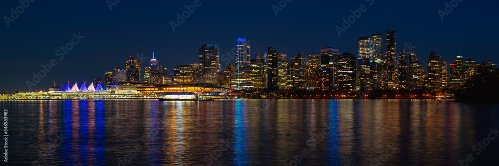 Naklejka premium Vancouver metropolitan skyline, buildings, and water reflections in blue, gold, and orange colors on Vancouver Harbor, night view of the city