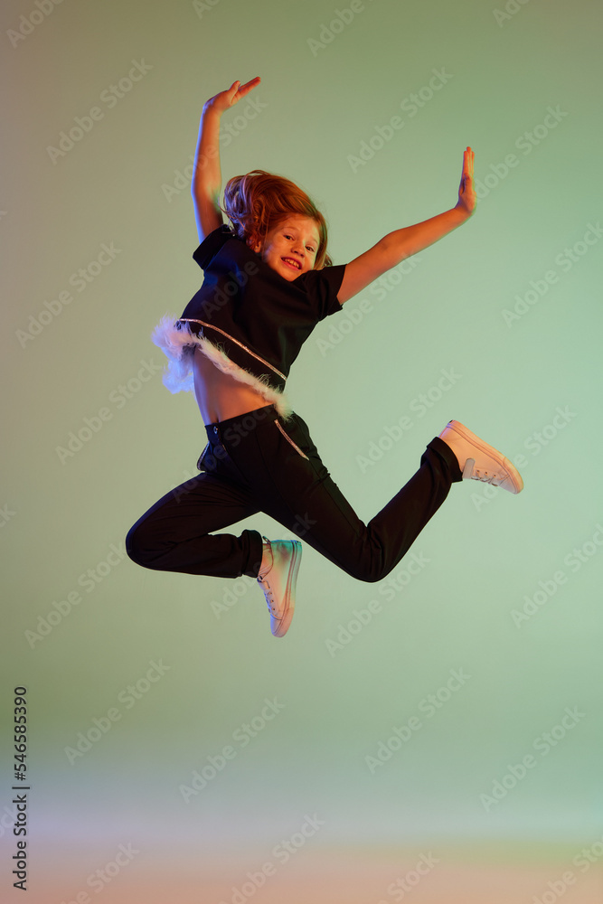 Dance, fun, joy. Happy little girl, kid in casual clothes jumping high isolated over light background. Kids fashion, emotions, carefree childhood - obrazy, fototapety, plakaty 