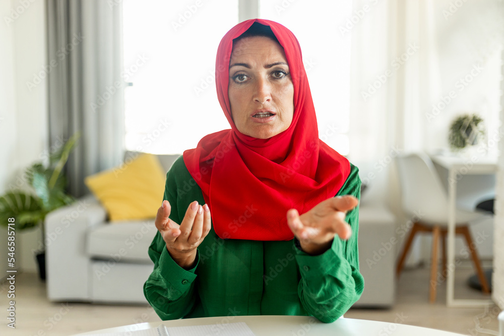 Mature islamic woman wearing hijab and talking to camera, communicating  online, sitting in living room Stock-Foto | Adobe Stock