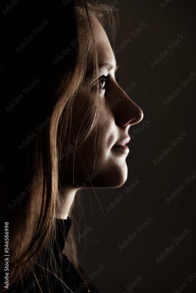 Close-up woman portrait in low light studio shot. Model face partly illuminated by light. Selective focus and image with shallow depth of field. Mysterious atmosphere. Toned image with brown color