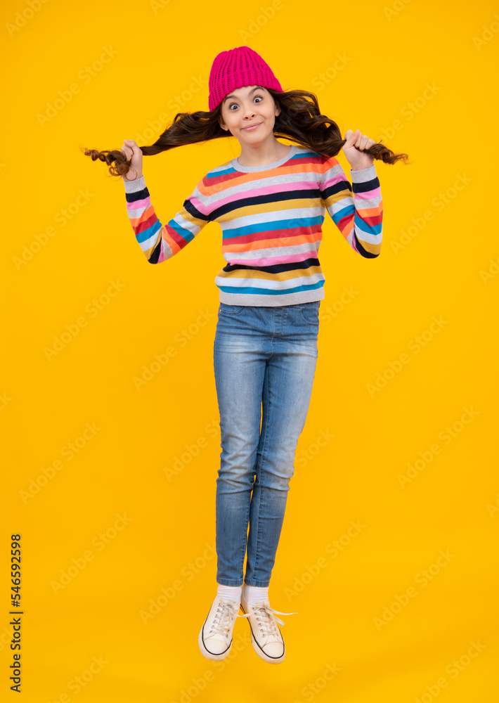Amazed teenager. Modern teenage girl 12, 13, 14 year old wearing sweater and knitted hat on isolated yellow background. Jump and run. Excited teen girl. Amazed teenager. Modern teenage girl 12, 13, 14 year old wearing sweater and knitted hat on isolated yellow background. Jump and run. Excited teen girl.