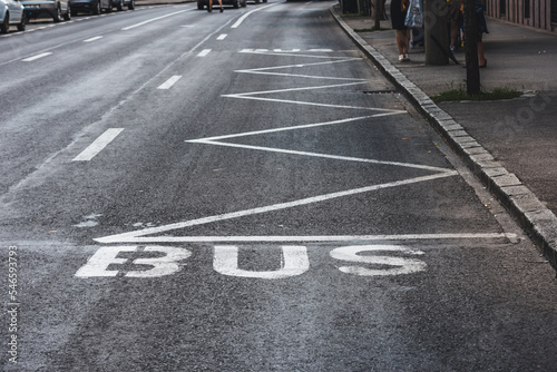 Bus road mark on black asphalt with a zig zag line to mark a bus station next to sidewalk