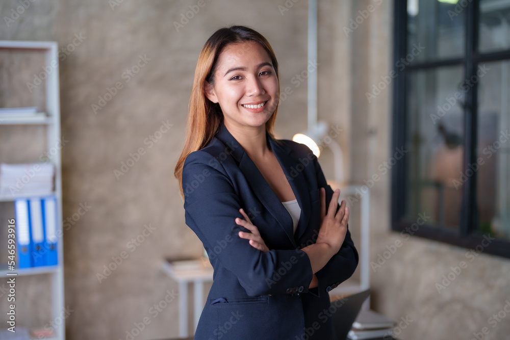 Asian businesswoman standing with her arms crossed and confidently looking at the camera and focused on her work in the office.
