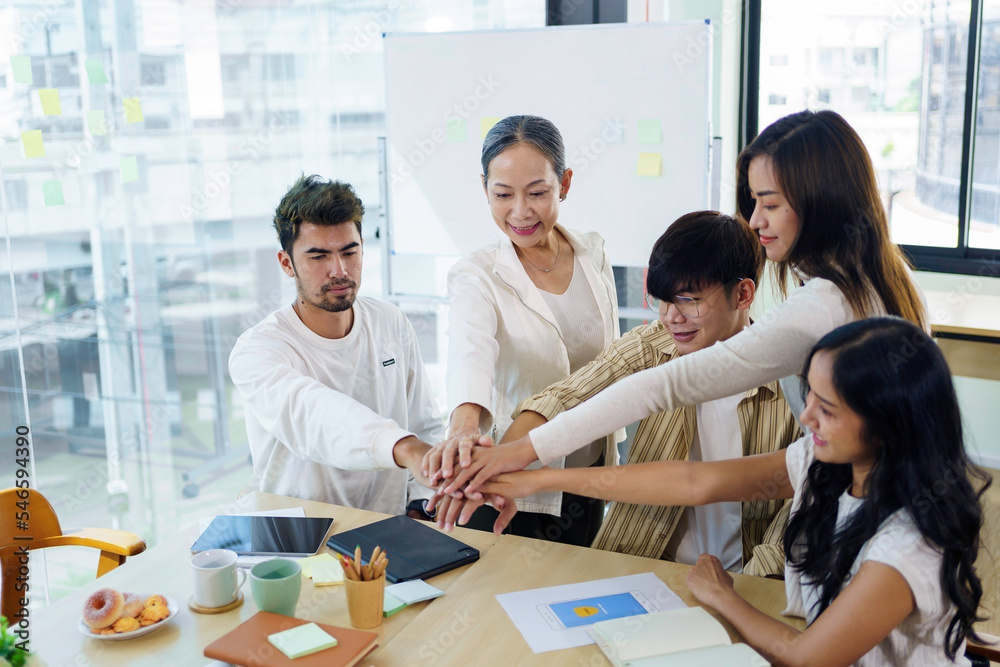 Young Asian business people shaking hands and working together as a team and having unity in working on new start-up project. Unity and Teamwork Concept. Young Asian business people shaking hands and working together as a team and having unity in working on new start-up project. Unity and Teamwork Concept.