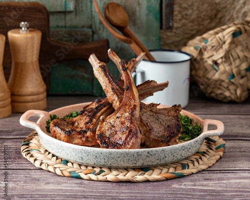 Fotografie Closeup of a tray of deliciously cooked lamb chops with herbs on a wooden surfac