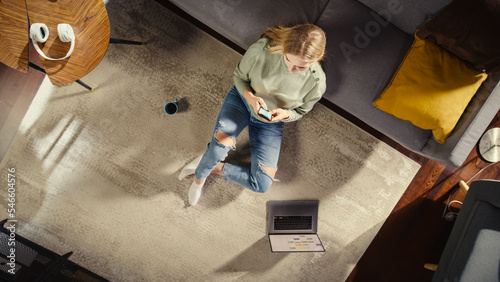 Apartment: Young Woman Uses Smartphone Sitting on Carpet in Living Room. Creative Freelancer Remote Work From Home. Entrepreneur doing E-business, Online Shopping, Social Media. Top View.