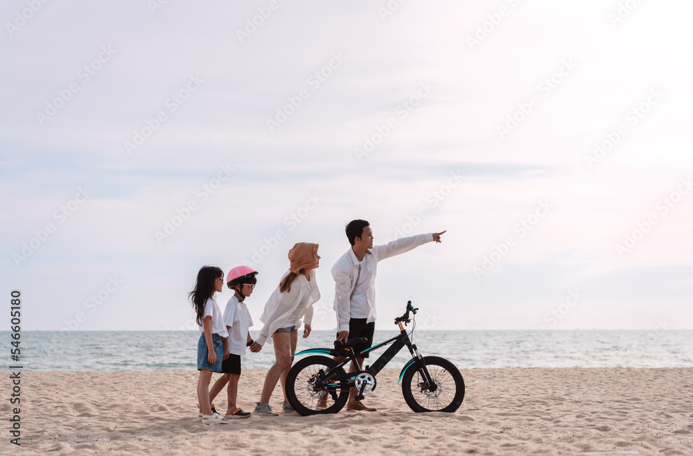 Fototapeta premium Family on the beach they are enjoy bicycle. Happy father, mother and son, daughter enjoying road trip the summer holidays.Parents and children are riding on a bicycle with a sea travel trip exercise