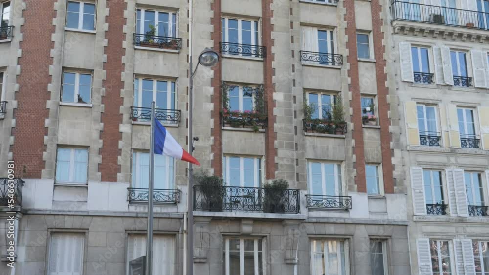 A panning shot of the residential building with the French flag on a pole.