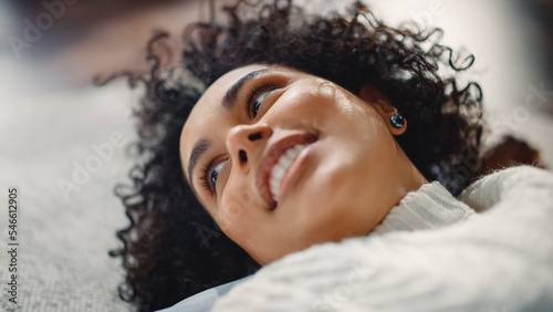 Close Up Portrait of Black Curly Female Talking with Somebody while Relaxing on the Floor at Home. Woman Plays with her Hair and Smiles Flirtaciously. Feeling of Falling in Love Concept.