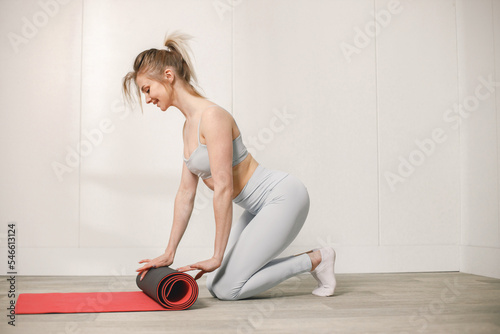 Portrait of a young woman in sportswear rolling a red mat after training
