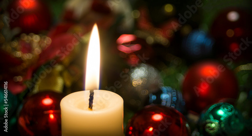 A lit candle in close-up along with Christmas ornaments photo