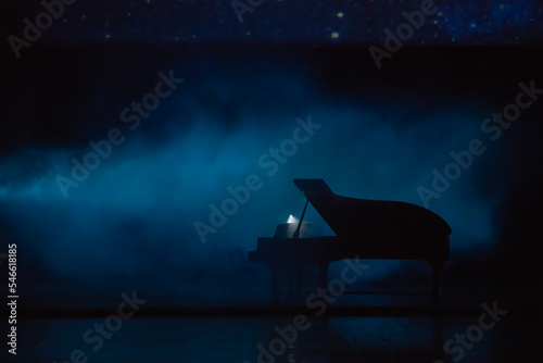 Piano in dramatic ambiance in concert hall, deep color. Silhouette pianon the empty scene