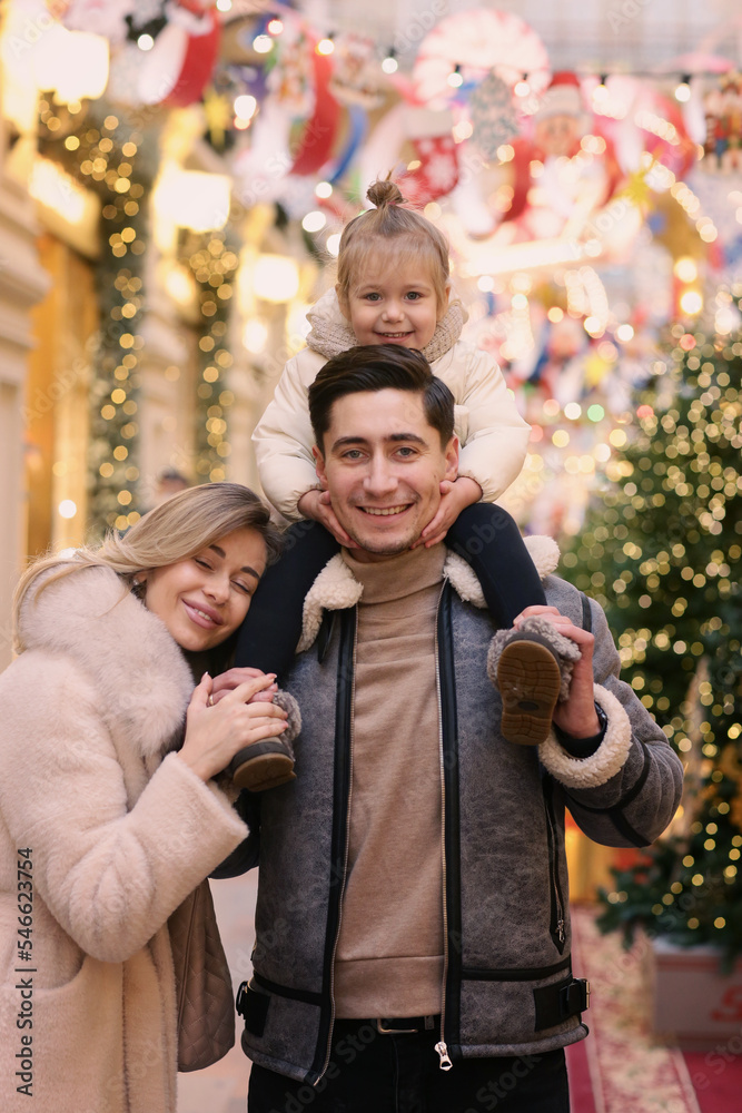 happy family mom dad and baby daughter on Christmas fair in big city shopping mall close up photo on illuminated decorations