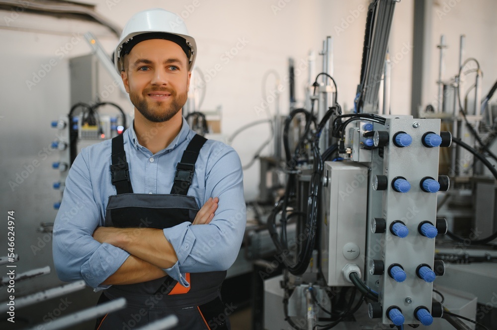 Portrait of factory worker in protective uniform and hardhat standing by industrial machine at production line. People working in industry Portrait of factory worker in protective uniform and hardhat standing by industrial machine at production line. People working in industry