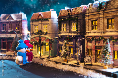 Snowmen on a nightly snow-covered street decorated for Christmas. Homemade decorated toy houses. © lizavetta
