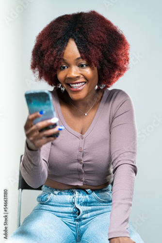giovane ragazza africana coni capelli afro seduta su una sedia e fa una video chiamata  photo