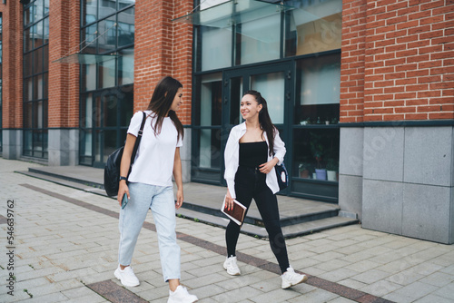 Positive female classmates walking on paved street