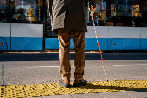 Blind man with a cane stopped on a tactile tile in front of a tram obstacle photo