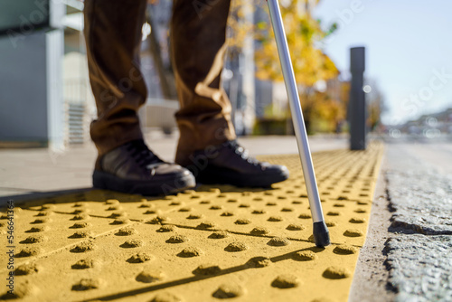 Close-up of a blind man with a walking stick. Stands on a tactile tile for self-orientation while moving through the streets of the city photo