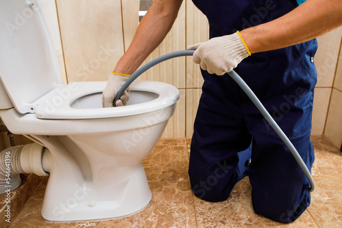 plumber unclogging blocked toilet with hydro jetting at home bathroom photo