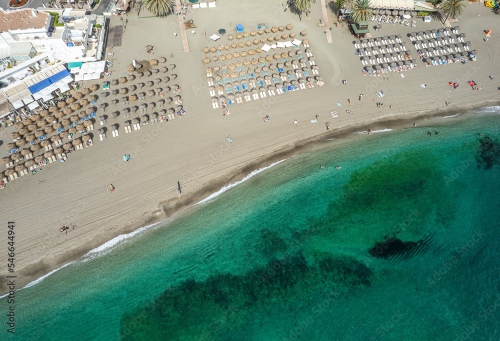View from above, aerial view of an emerald and transparent Mediterranean sea with the beach full of beach umbrellas and tourists who relax and swim. Marbella, Spain.
