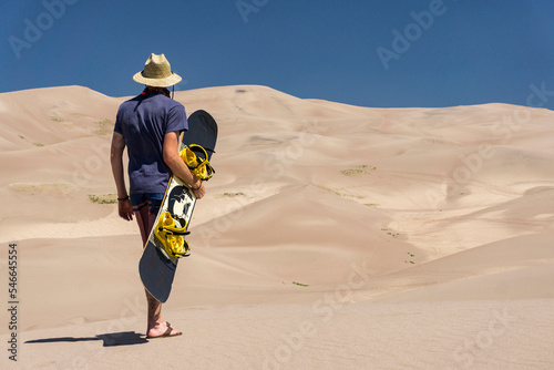 Male hiking through sand dunes with a snowboard photo