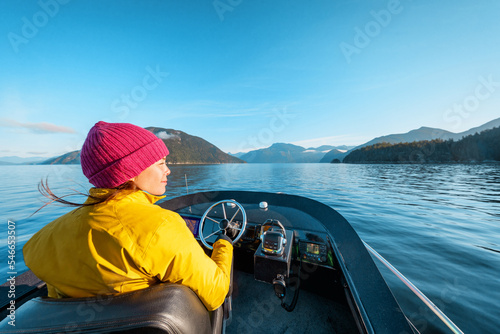 Woman Driving Motor Boat in Beautiful Nature Landscape Smiling Happy at Sunset in Coastal British Columbia Near Bute, Toba Inlet, and Campbell River. Whale Watching Tourist Travel Destination, Canada photo