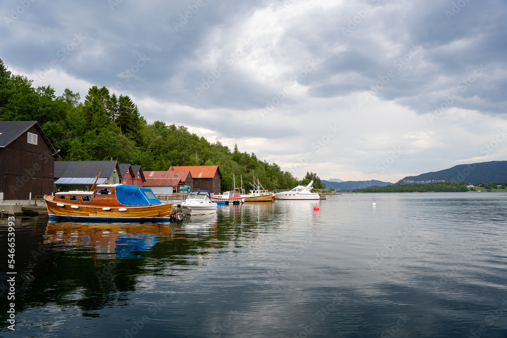 a small boat dock on the shore of a fabulous fjord with green mountains and a beautiful sky, the boat is tied to the footbridge and the boat house is in the background