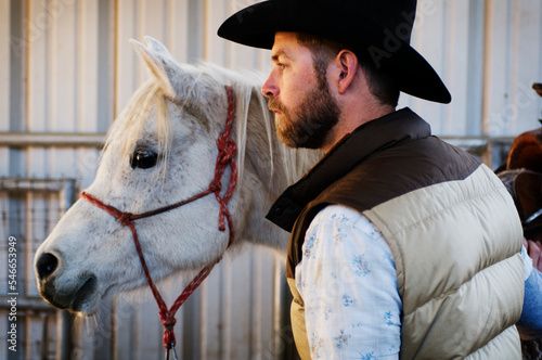 A male ranch hand in a cowboy hat strokes the neck of Nell, a four year old arabian mare, and gets ready to go out on a horseback ride in Flagstaff, AZ. photo