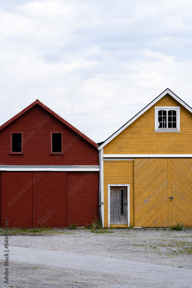 red and yellow fisherman's shed in Norway, which runs one over the other and has a beautiful view above it, but in the foreground there are some weeds growing between the gray gravel of the yard red and yellow fisherman's shed in Norway, which runs one over the other and has a beautiful view above it, but in the foreground there are some weeds growing between the gray gravel of the yard