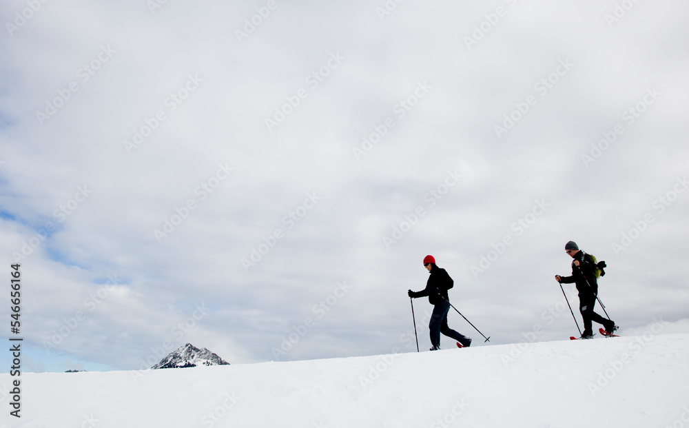 Two people snow shoeing along a ridge on an overcast day. Two people snow shoeing along a ridge on an overcast day.