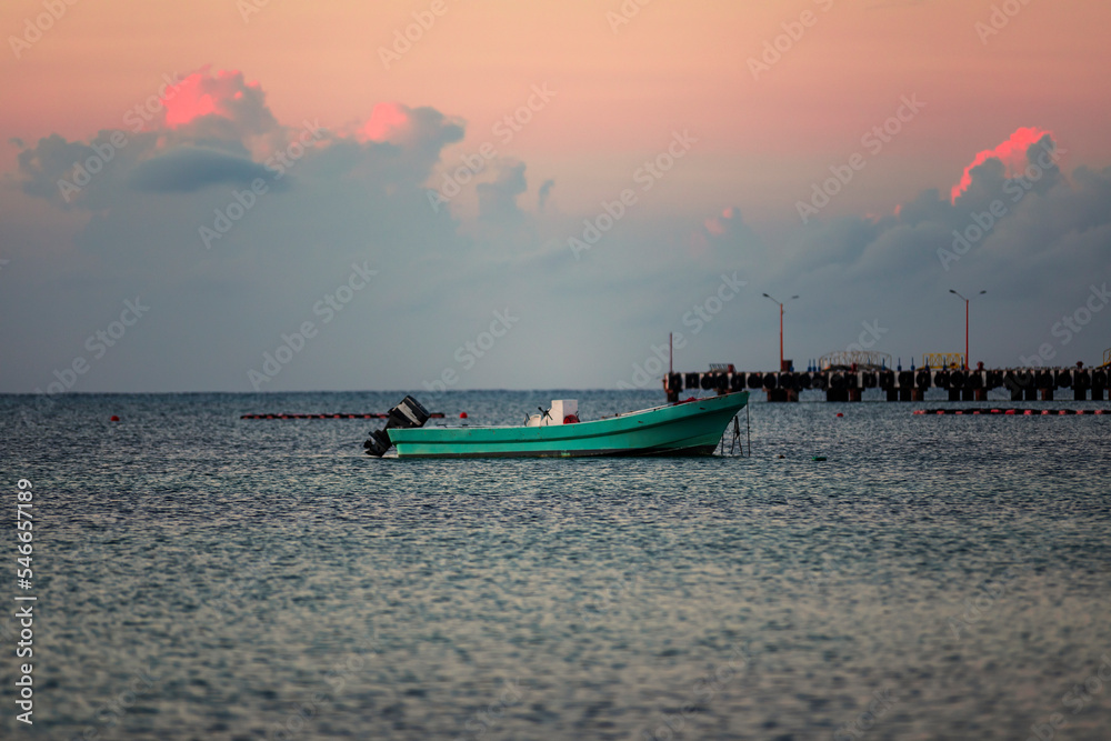Colorful sunrise at the magic hour of the day in the caribbean sea with a boat in the ocean water, beautiful colorful photo with a warm sky and clouds.