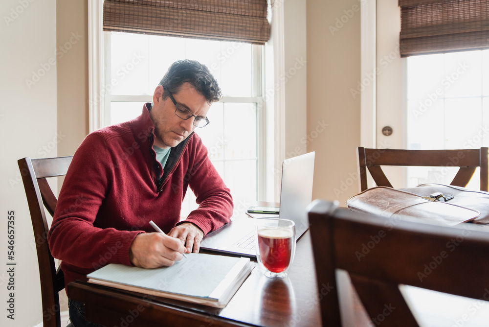 Man in glasses working from home using a computer at a dining table. Man in glasses working from home using a computer at a dining table.
