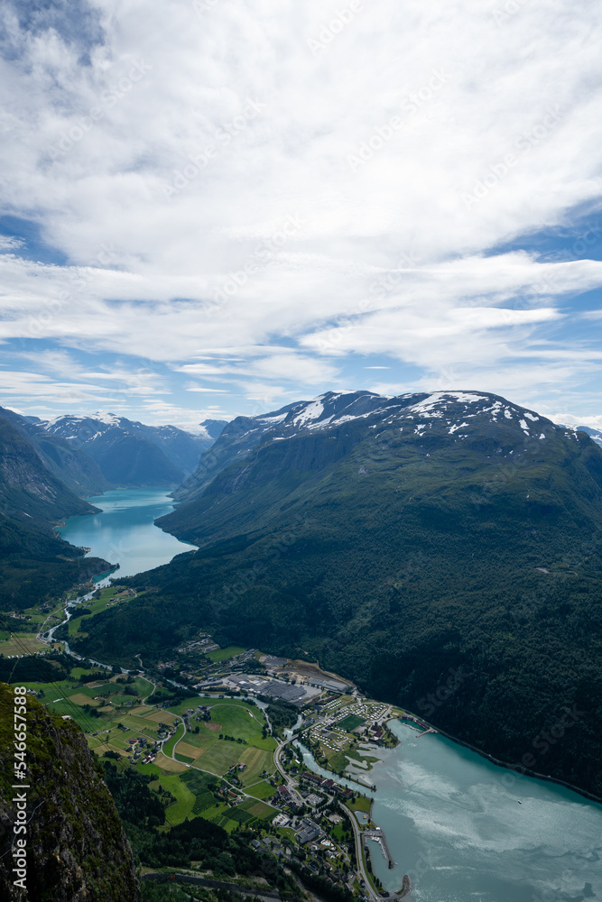 Norwegian mountain landscape from a high mountain down in the valley there is a village and in the distance between the mountain you can see a fjord with blue water above