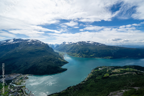 Norwegian mountain landscape from a high mountain down in the valley there is a village and in the distance between the mountain you can see a fjord with blue water above which there is beautiful sky © Rolands