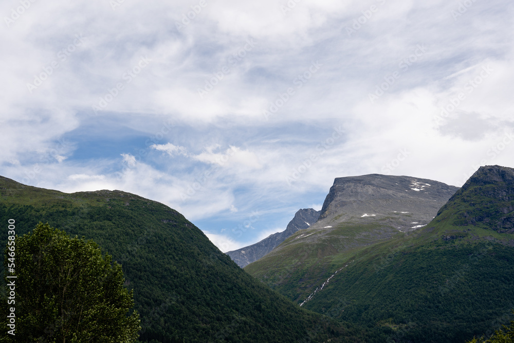 the dark mountains of Norway, covered with green moss, but above the rocky mountain tops is a blue sky with saturated white and gray clouds
