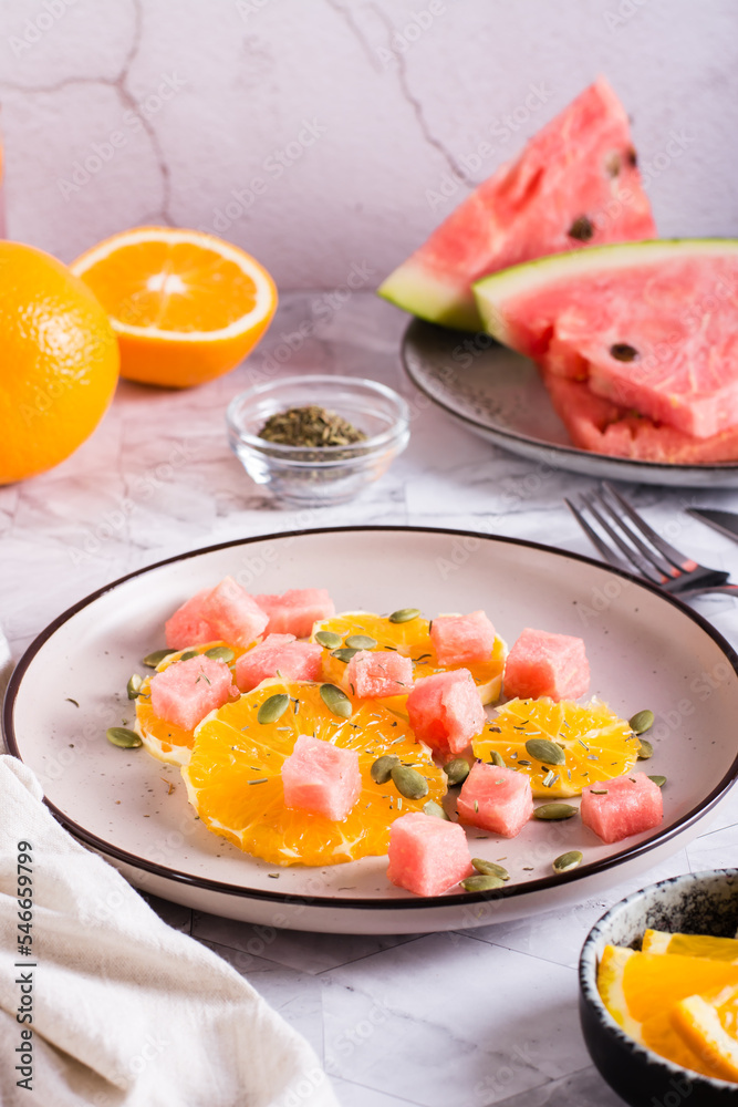 Fruit salad of watermelon, orange and pumpkin seeds on a plate on the table. Healthy food. Vertical
