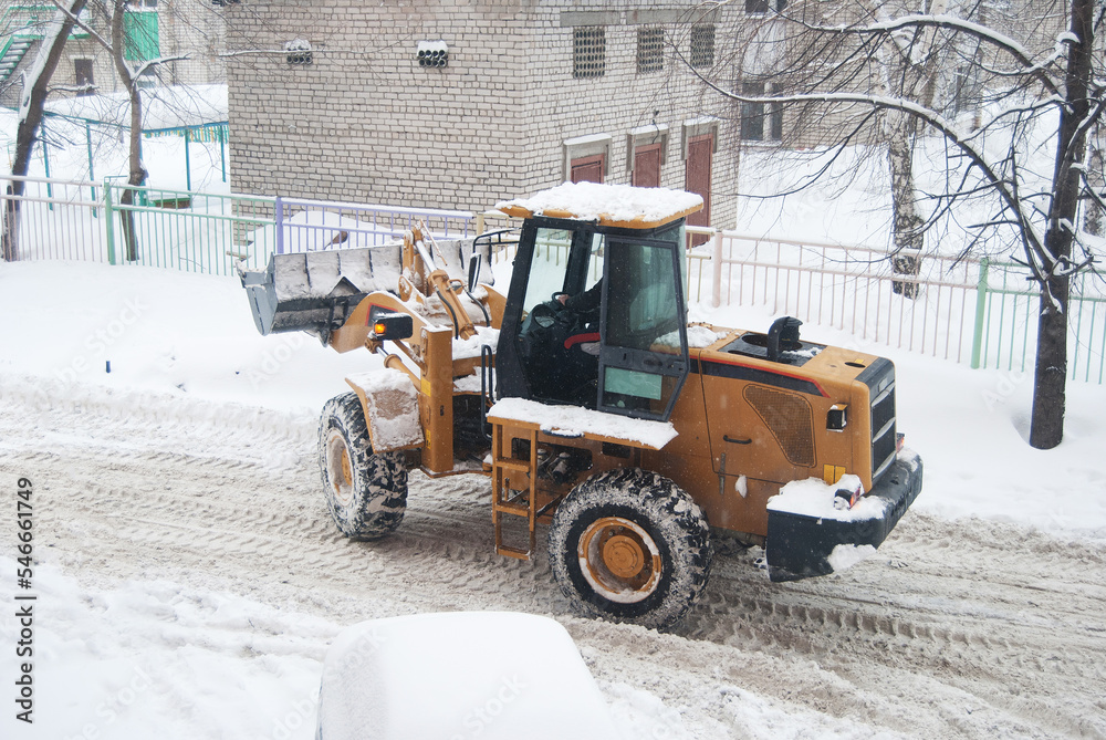 yellow excavator removes snow from the street