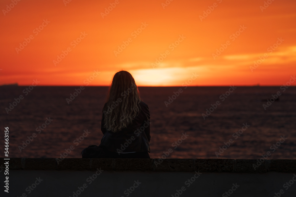 Woman alone looking at the colorful sunset at La Caleta in Cadiz, Andalusia, Spain