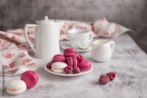 Sweet still life: macaroons with raspberries and a coffee service on a light marble table. Greeting concept for mother's day, international women's day or good morning wishes. Selective focus. 
