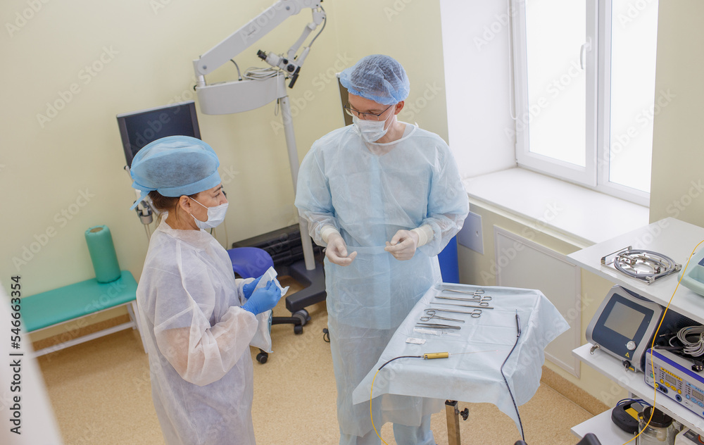 a male surgeon, together with an assistant, lays out sterile instruments to prepare for surgery.
