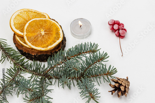 Slices of dry orange on a stump. A sprig of spruce, cones and a burning candle.