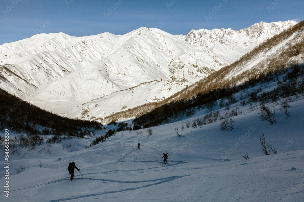 A team of freerider skiers climbs against the background of snowy ridges of the Caucasus Mountains, Svaneti, Georgia, backcountry