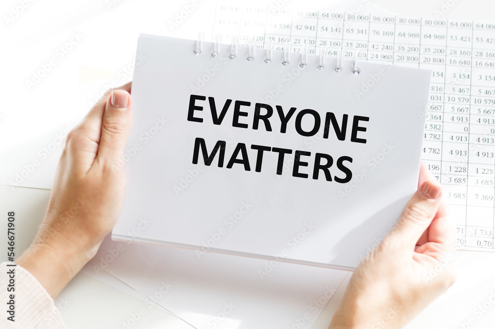 EVERYONE MATTERS text on a notebook in the hands of a person on the background of an office desk EVERYONE MATTERS text on a notebook in the hands of a person on the background of an office desk