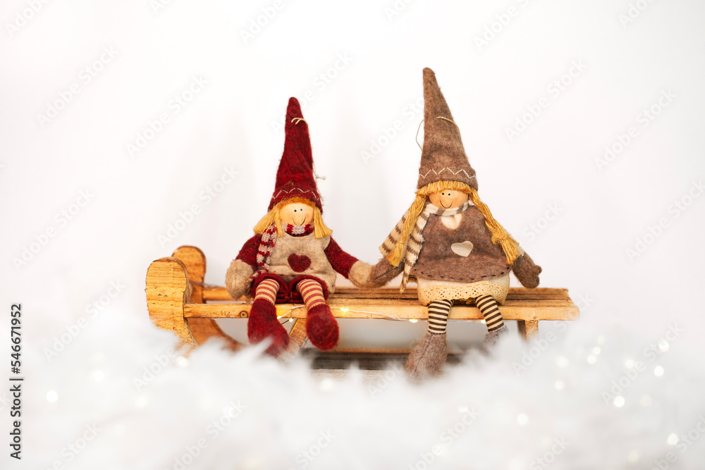 Christmas toys - girl and boy gnomes sitting on a sledge on snowy white background