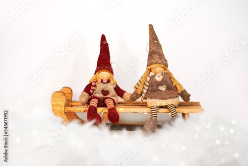 Christmas toys - girl and boy gnomes sitting on a sledge on snowy white background