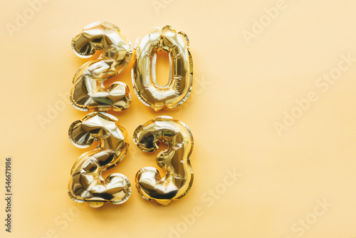 Vertically arranged balloons made of gold foil in the form of the numbers 2023 on a yellow background. Celebrating Christmas, New Year and festive concept. Flat position, top view.