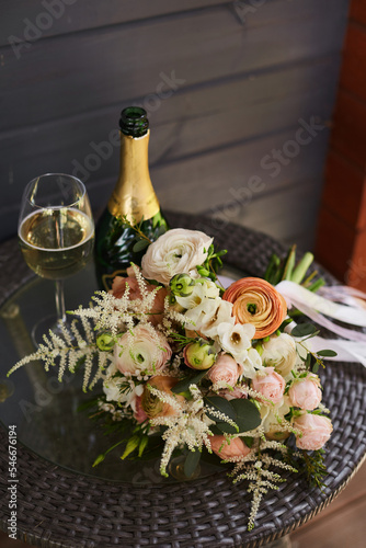 Glass of champagne on a background of flowers. Wedding bouquet of the bride. Bridal bouquet of calla flowers and green branches. Bridal bouquet lies on a wooden table with a glass. The morning of the photo