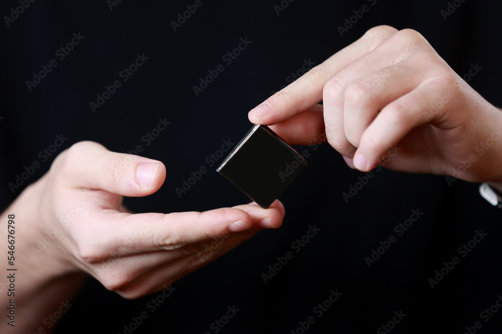 Mans hands holding a square little black box with an copy empty space for text and design isolated on dark background. Board, blank, template, mockup, layout for a slogan or inscription. Mans hands holding a square little black box with an copy empty space for text and design isolated on dark background. Board, blank, template, mockup, layout for a slogan or inscription.