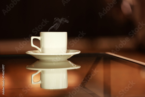 Mockup white cup with hot drink and steam on a mirror table with copy space. Hot steaming mug of coffee or tea with a mirror image. Blank template for your design, branding, business.